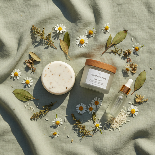 Flat lay of tear stain bundle with shampoo bar, face mask jar, chamomile and brightening botanicals on sage green linen